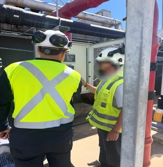 Profesionales con casco y chaleco revisando un tablero de control en terreno